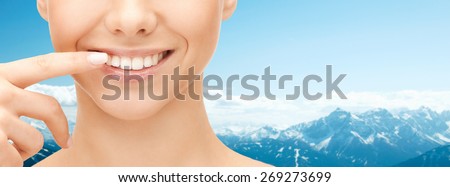 dental health, beauty, hygiene and people concept - close up of smiling woman face pointing to teeth over blue mountains background