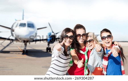 summer holidays, vacation, travel and people concept - happy teenage girls in sunglasses or young students showing thumbs up over airport background