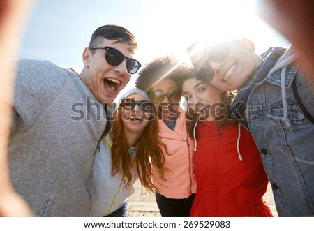 tourism, travel, people, leisure and technology concept - group of happy laughing teenage friends taking selfie outdoors