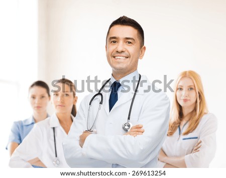 healthcare, profession, people and medicine concept - smiling male doctor in white coat over group of medics at hospital background