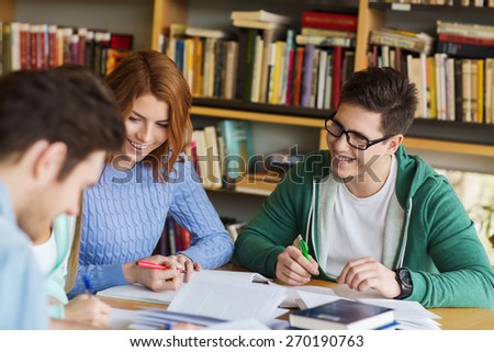 people, knowledge, education and school concept - group of happy students with books preparing to exam and writing in library
