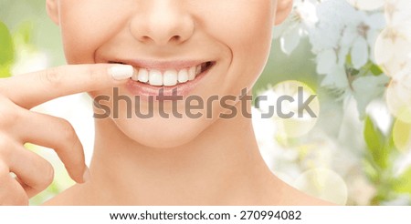 dental health, beauty, hygiene and people concept - close up of smiling woman face pointing to teeth over green natural background