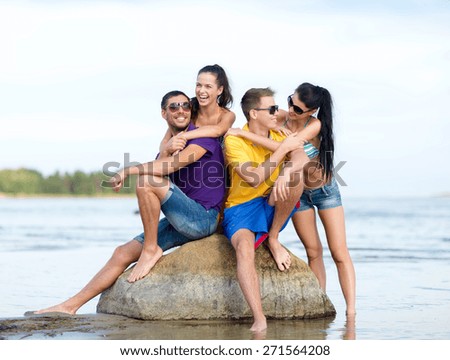 friendship, sea, summer holidays, beach and people concept - group of happy friends sitting on rock