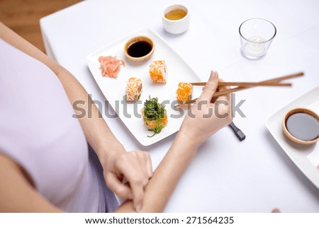 restaurant, food, people, asian and japanese kitchen concept - close up of woman eating sushi with chopsticks at restaurant