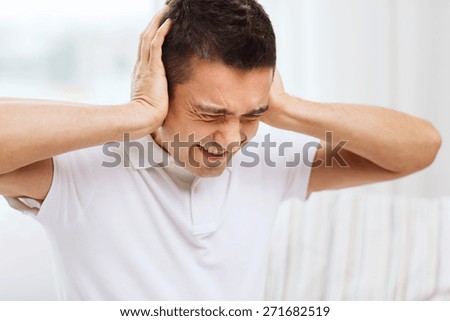 people, crisis, emotions, noise and stress concept - unhappy man closing his ears by hands at home