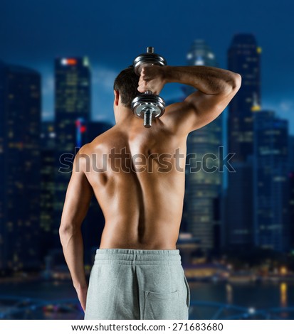 sport, fitness, weightlifting, bodybuilding and people concept - young man with dumbbell flexing biceps over night city background from back