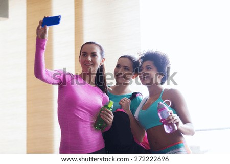 fitness, sport, training, gym and lifestyle concept - group of happy women with bottles and smartphone taking selfie in gym