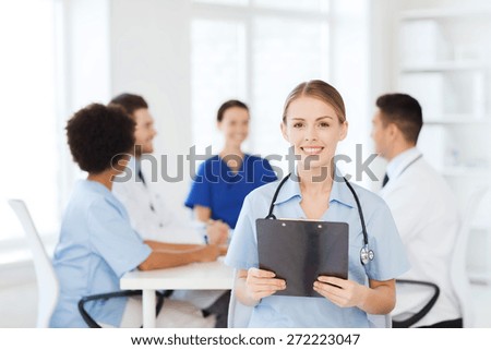 clinic, profession, people and medicine concept - happy female doctor with clipboard over group of medics meeting at hospital