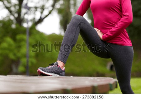fitness, sport, training, people and lifestyle concept - close up of woman stretching leg and doing lunge on bench in park