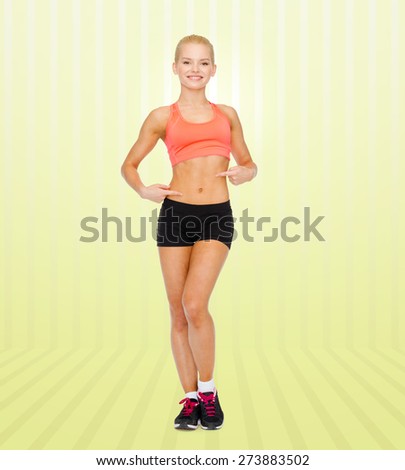 fitness, sport, people and weight loss concept - smiling beautiful sporty woman pointing at her six pack over yellow striped background