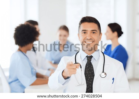 clinic, profession, people and medicine concept - happy male doctor over group of medics meeting at hospital pointing to you