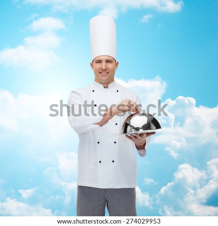 cooking, profession and people concept - happy male chef cook holding cloche over blue sky with clouds background