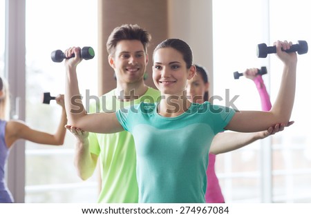 fitness, sport, training, gym and lifestyle concept - group of happy women and trainer with dumbbells flexing muscles in gym