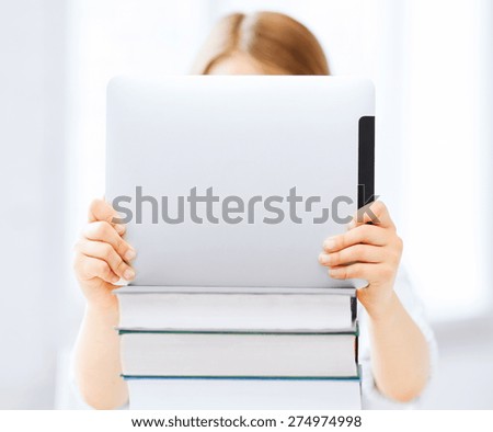 education, school, technology and internet concept - little student girl hiding behind tablet pc and books at school