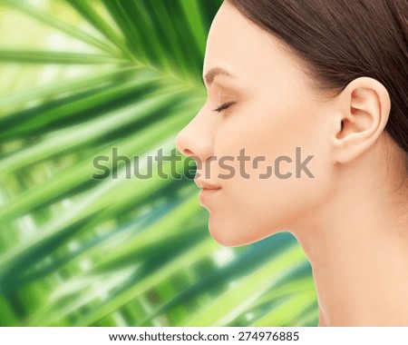health, people, eco and beauty concept - beautiful young woman face over green palm leaf background