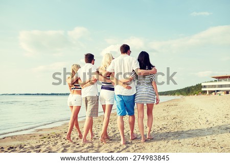 summer, holidays, sea, tourism and people concept - group of smiling friends hugging and walking on beach from back