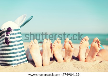 summer vacation, sunbathing and pedicure concept - three women lying on the beach with straw hat, sunglasses and bag