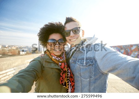 tourism, travel, people, leisure and technology concept - happy teenage international couple taking selfie on city street