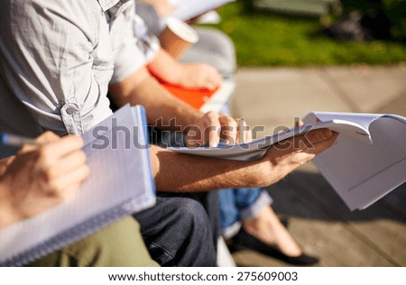 summer, friendship, education and teenage concept - close up of students with notebooks reading and writing at campus