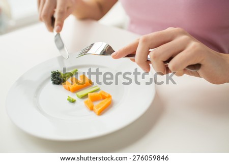 healthy lifestyle, diet, vegetarian food and people concept - close up of woman with fork and knife eating vegetable letters on plate