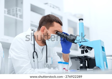 science, medicine, technology, biology and people concept - young male scientist with test tubes looking to microscope and making or research in clinical laboratory