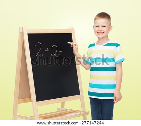 people, school, children, mathematics and education concept - happy little boy with blackboard and chalk writing math exercise over yellow background