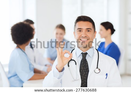 clinic, profession, people and medicine concept - happy male doctor over group of medics meeting at hospital showing ok hand sign