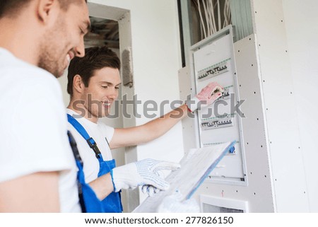 business, building, teamwork and people concept - group of smiling builders with clipboard and electrical panel indoors