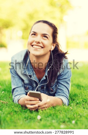 lifestyle, summer vacation, technology, leisure and people concept - smiling young girl with smartphone and earphones lying on grass