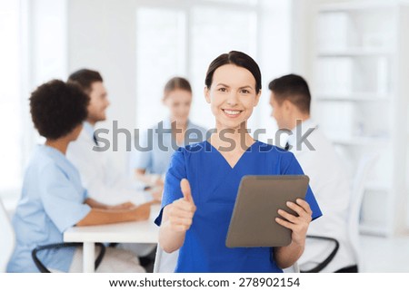 clinic, profession, people and medicine concept - happy female doctor with tablet pc computer over group of medics meeting at hospital showing thumbs up gesture