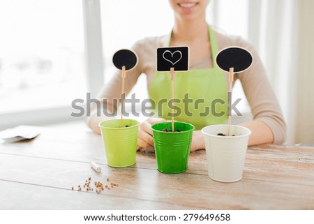 people, gardening, seeding and profession concept - close up of woman over pots with soil and signs