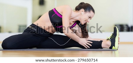 fitness, sport, training, gym and lifestyle concept - smiling teenage girl with earphones stretching on mat in the gym