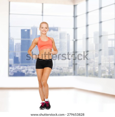 fitness, sport, people and weight loss concept - smiling beautiful sporty woman pointing at her six pack over gym background