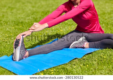 fitness, sport, training, people and lifestyle concept - close up of woman stretching leg on mat in park
