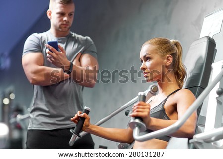 sport, fitness, bodybuilding, teamwork and people concept - young woman and personal trainer flexing muscles on gym machine