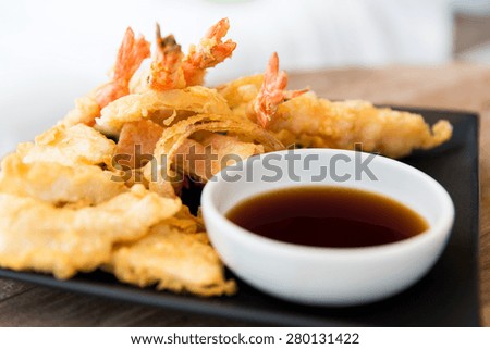 asian kitchen, food, culinary and cooking concept - close up of deep-fried tempura shrimps with soy sauce on table at restaurant