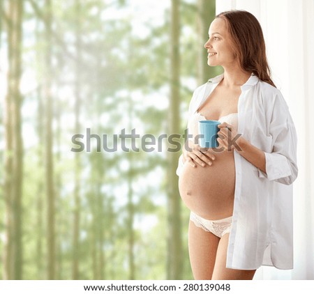 pregnancy, drinks, rest, people and expectation concept - happy pregnant woman in shirt and underwear with cup drinking tea over woods background
