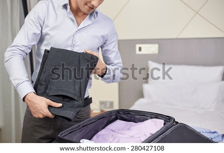 business, trip, luggage and people concept - happy businessman packing clothes into travel bag