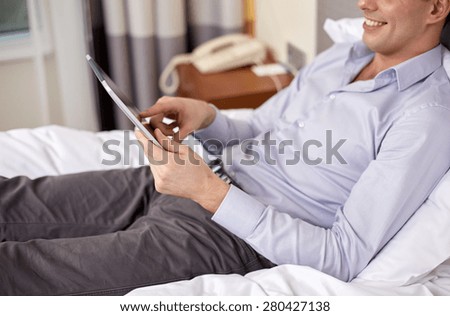 business trip, technology, internet and people concept - smiling businessman with tablet pc computer lying on bed at hotel room