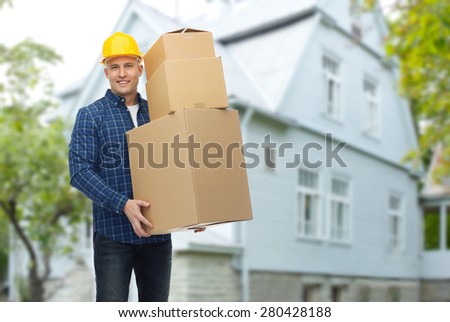 repair, building, construction, loading and delivery concept - smiling man or loader in helmet with cardboard boxes over living house background