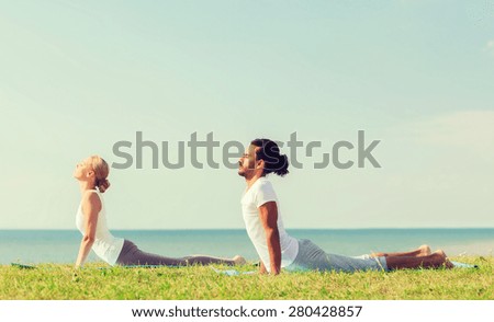 fitness, sport, friendship and lifestyle concept - smiling couple making yoga exercises lying on mats outdoors