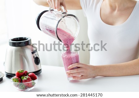 healthy eating, cooking, vegetarian food, dieting and people concept - close up of woman with blender and strawberries pouring milk shake to glass at home