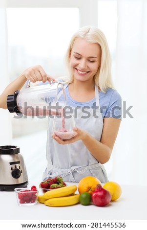 healthy eating, cooking, vegetarian food, dieting and people concept - smiling young woman putting fruits for fruit shake to blender shaker at home