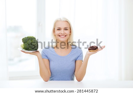 healthy eating, junk food, diet and choice people concept - smiling woman choosing between broccoli and donut at home