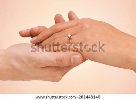 jewelry, couple, love and wedding concept - close up of man and woman hands with engagement ring over beige background