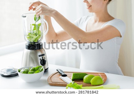 healthy eating, cooking, vegetarian food, dieting and people concept - close up of young woman with blender and green vegetables making detox shake or smoothie at home