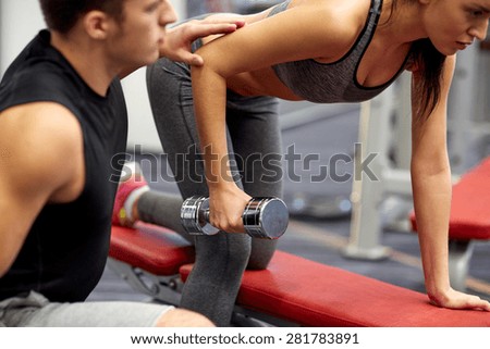 fitness, sport, exercising and weightlifting concept - close up of young woman and personal trainer with dumbbells flexing muscles in gym