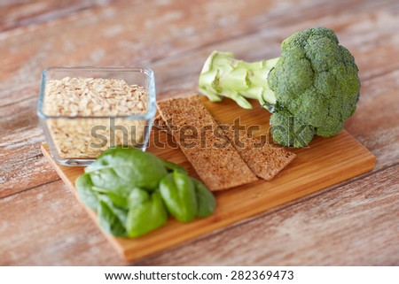 healthy eating, diet and fiber rich in food concept - close up of broccoli, crispbread, oatmeal and spinach on wooden table