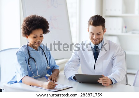 hospital, profession, people and medicine concept - two happy doctors with tablet pc computer meeting and talking at medical office