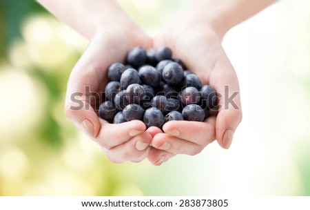 healthy eating, dieting, vegetarian food and people concept - close up of woman hands holding blueberries over green natural background